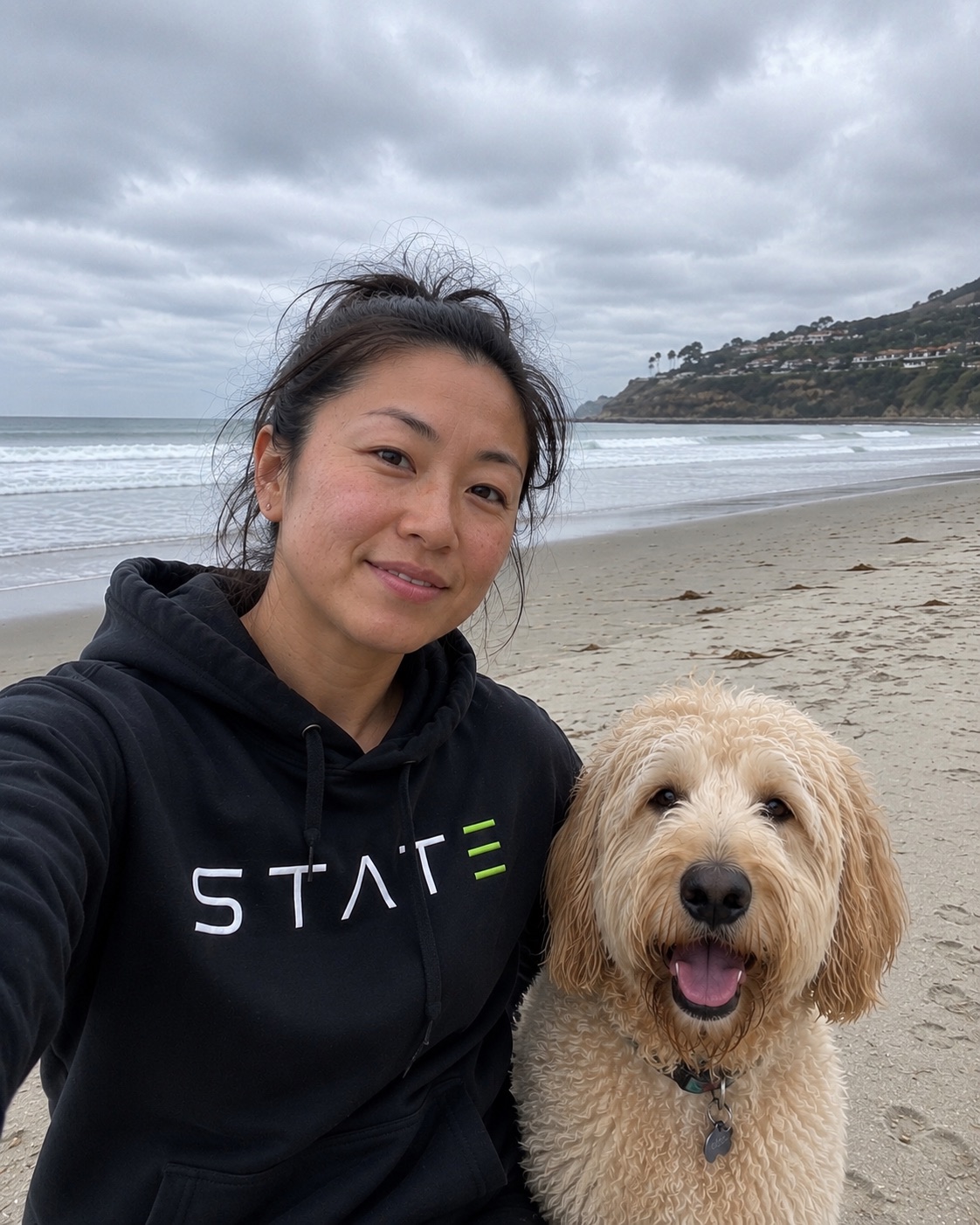 Person wearing a black STATE hoodie on the beach